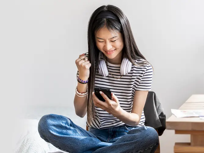A girl looking at her phone, fist-bumping with a smile on her face